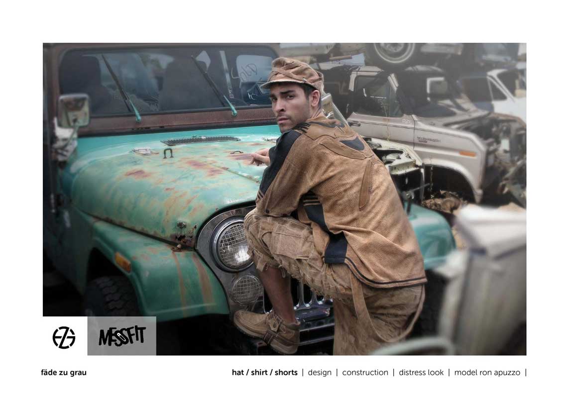 male fashion model in a junk yard presents brown hat, brown shirt and brown shorts