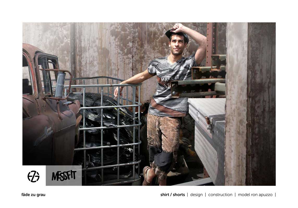 male fashion model in a junk yard presents gray brown t-shirt and brown shorts