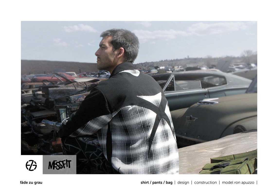 male fashion model in a junk yard presents black and white shirt with X on back
